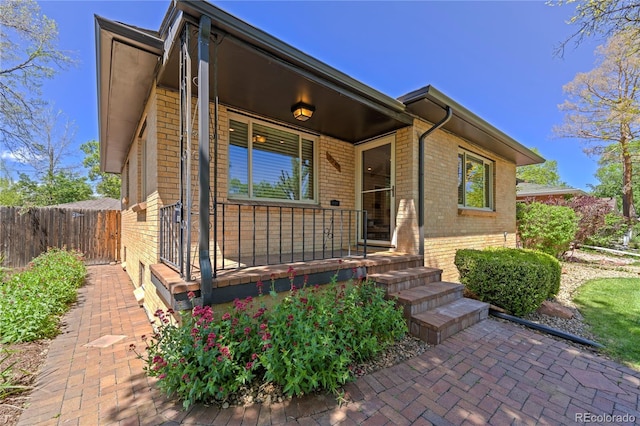 view of front of house with brick siding, covered porch, and fence