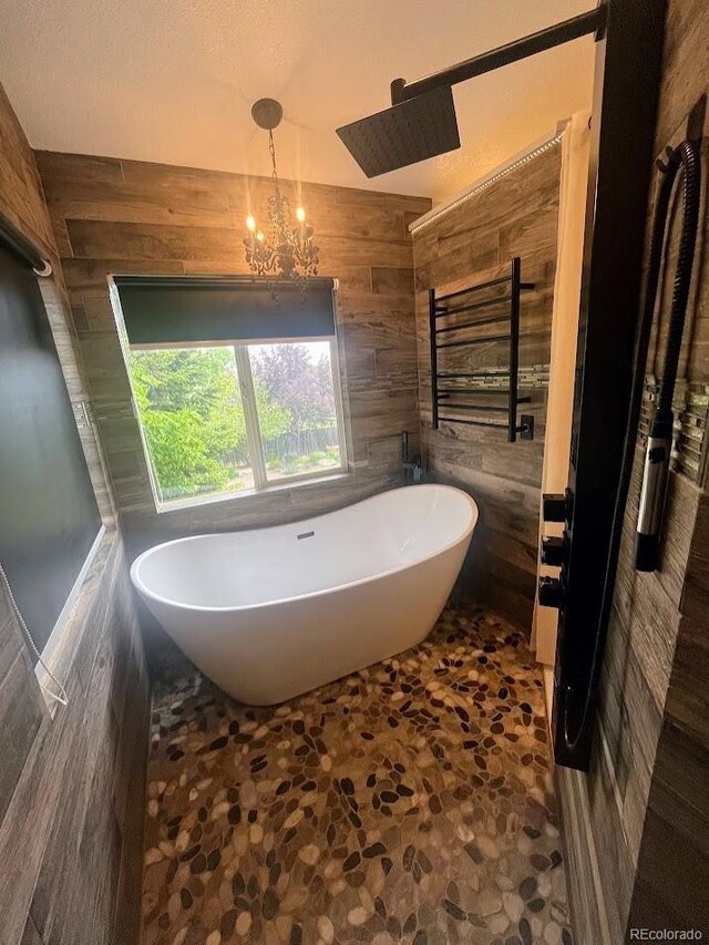 12742 Clermont St, Thornton, CO 80241 - bathroom with a freestanding tub, wooden walls, stone flooring, a towel warming rack, and a chandelier