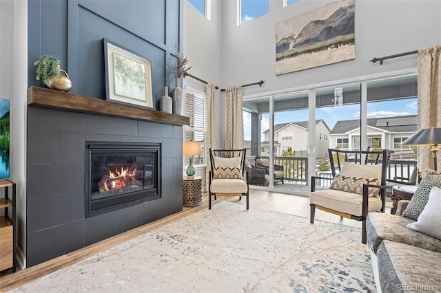 living area with a tile fireplace, a towering ceiling, and light wood-type flooring