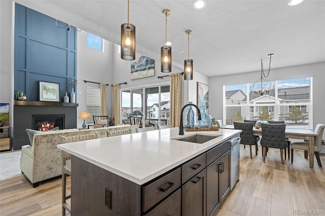 kitchen with dishwasher, an island with sink, sink, a large fireplace, and dark brown cabinets