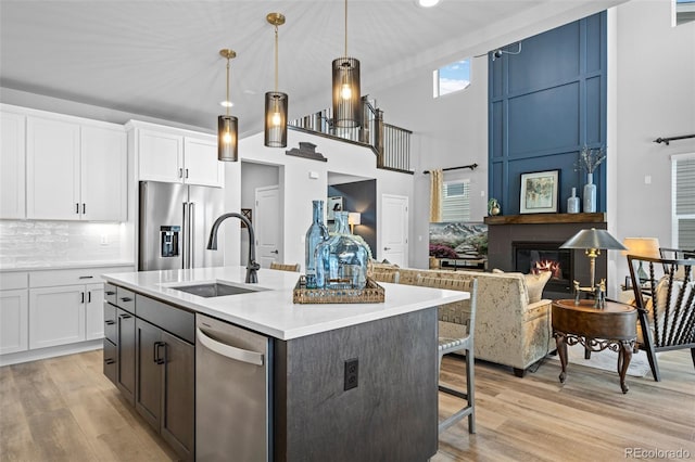 kitchen with appliances with stainless steel finishes, pendant lighting, an island with sink, sink, and white cabinets