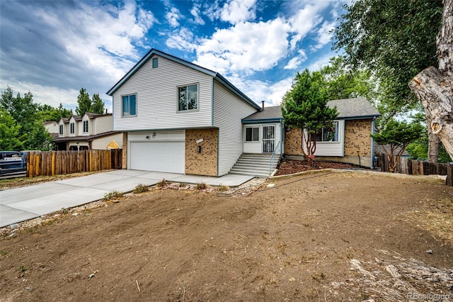 split level home with a garage, fence, brick siding, and driveway