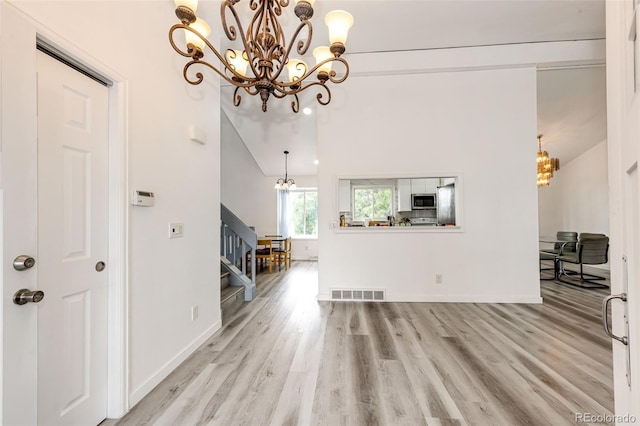 unfurnished living room featuring stairway, a notable chandelier, wood finished floors, and visible vents