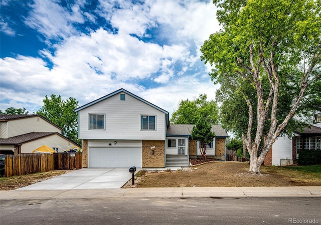 split level home with a garage, brick siding, concrete driveway, and fence