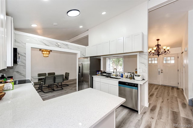 kitchen with a peninsula, stainless steel appliances, an inviting chandelier, white cabinetry, and a sink