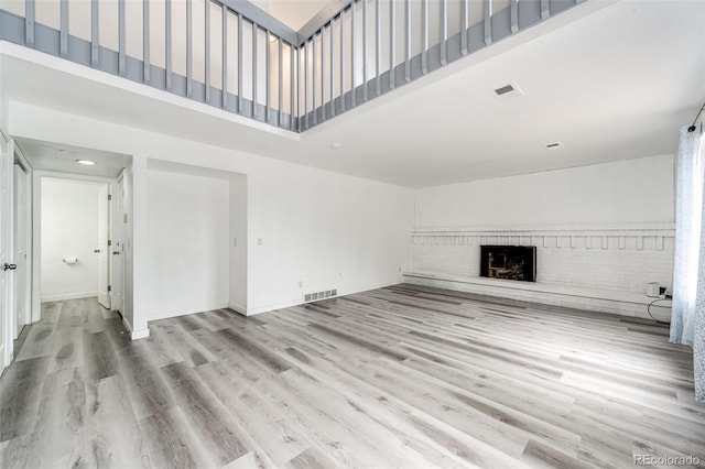 unfurnished living room featuring visible vents, a high ceiling, wood finished floors, and a fireplace