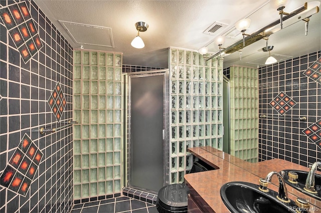 bathroom with tile patterned floors, tile walls, a shower with door, and a textured ceiling