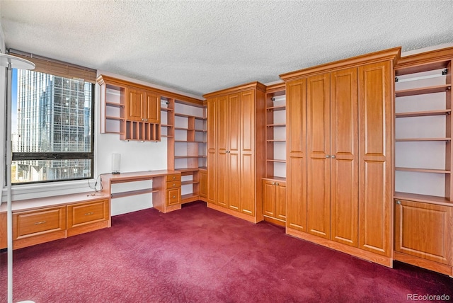 unfurnished office with built in desk, a textured ceiling, and dark colored carpet