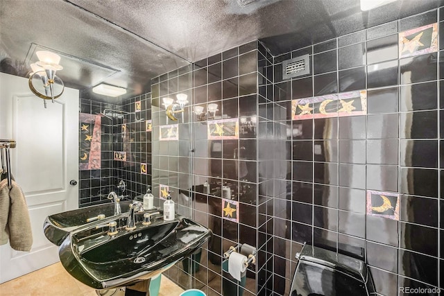 bathroom with a textured ceiling, tile walls, and sink