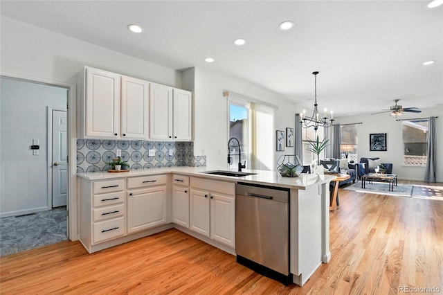 kitchen featuring white cabinetry, a peninsula, a sink, stainless steel dishwasher, and open floor plan