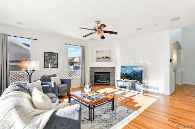 living area with wood finished floors, visible vents, a fireplace, arched walkways, and ceiling fan