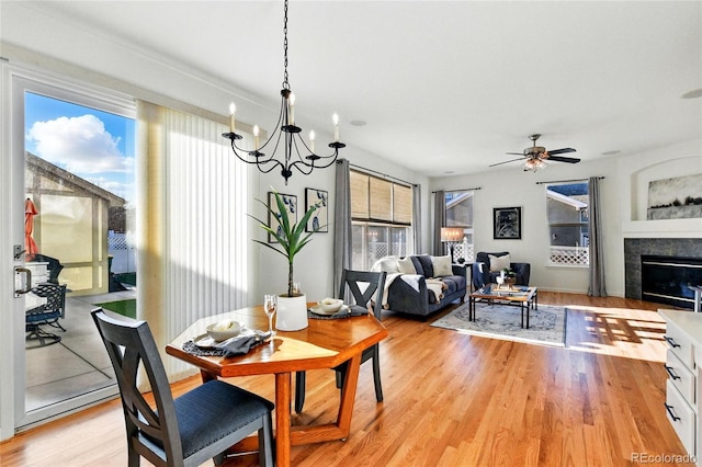 dining area with a glass covered fireplace, light wood-style flooring, and ceiling fan with notable chandelier