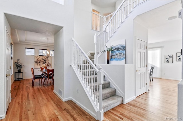 stairway with a chandelier, a towering ceiling, baseboards, and wood finished floors