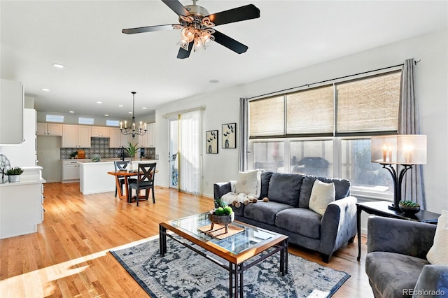 living room featuring recessed lighting, light wood-style flooring, and ceiling fan with notable chandelier