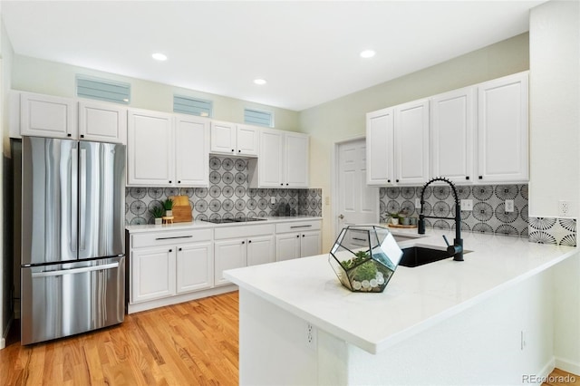 kitchen with a peninsula, freestanding refrigerator, white cabinets, black electric stovetop, and light wood-type flooring