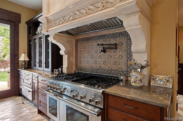 kitchen with backsplash, range with two ovens, dark stone counters, and custom exhaust hood