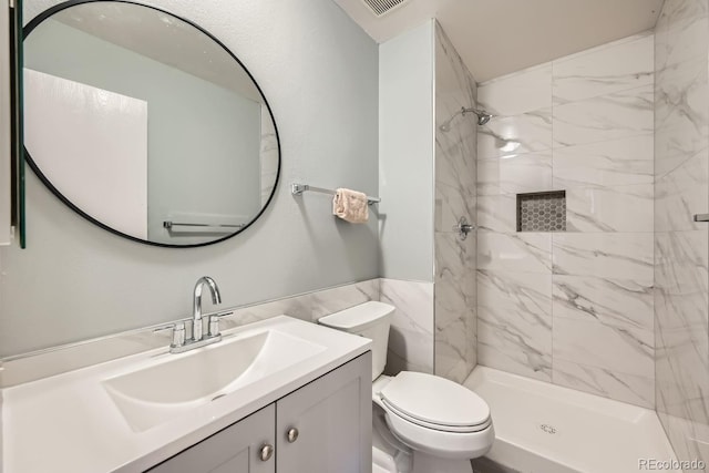 bathroom featuring toilet, tiled shower, and vanity