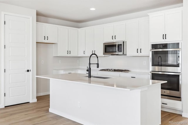 kitchen with appliances with stainless steel finishes, a center island with sink, white cabinetry, and light hardwood / wood-style floors