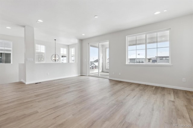 unfurnished living room featuring plenty of natural light, a notable chandelier, and light hardwood / wood-style flooring