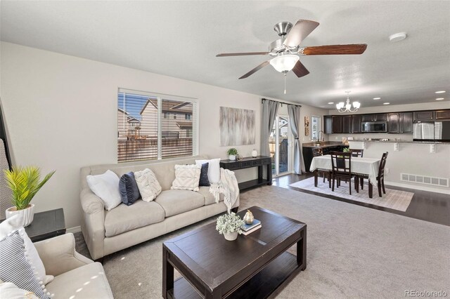 carpeted living room with ceiling fan with notable chandelier