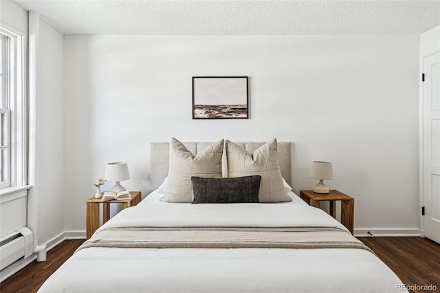 bedroom with multiple windows, dark wood-type flooring, a baseboard radiator, and a textured ceiling