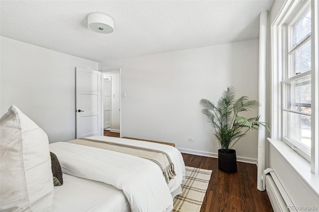 bedroom featuring baseboard heating, multiple windows, dark wood-type flooring, and a textured ceiling