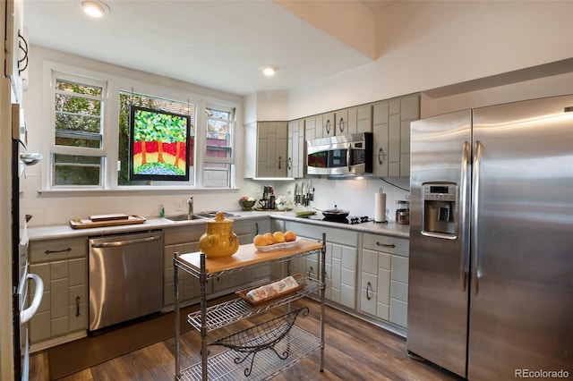 kitchen featuring appliances with stainless steel finishes, backsplash, gray cabinetry, dark wood-type flooring, and sink