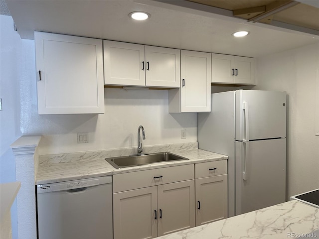 kitchen with white appliances, a sink, white cabinets, recessed lighting, and light stone countertops