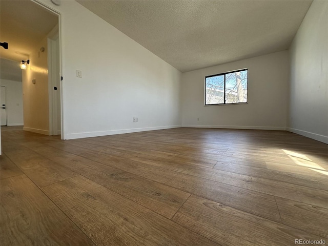 spare room featuring hardwood / wood-style flooring, a textured ceiling, baseboards, and lofted ceiling