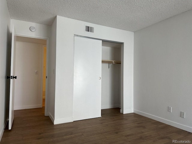 unfurnished bedroom featuring dark wood-style floors, a closet, a textured ceiling, and baseboards