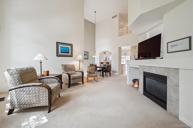 living area featuring a fireplace, arched walkways, carpet, a towering ceiling, and visible vents