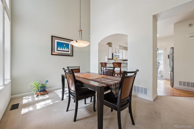 dining room with visible vents, arched walkways, a high ceiling, and light carpet