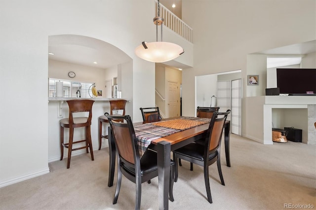 dining space with arched walkways, baseboards, light colored carpet, and a towering ceiling