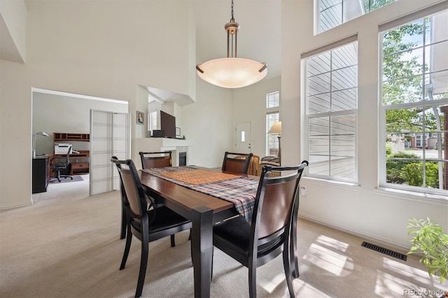 dining area with visible vents, a towering ceiling, a fireplace, baseboards, and light carpet