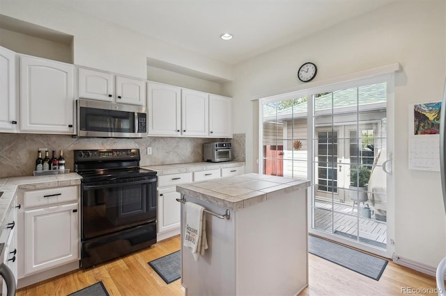 kitchen with black electric range oven, light wood-style flooring, white cabinetry, stainless steel microwave, and decorative backsplash