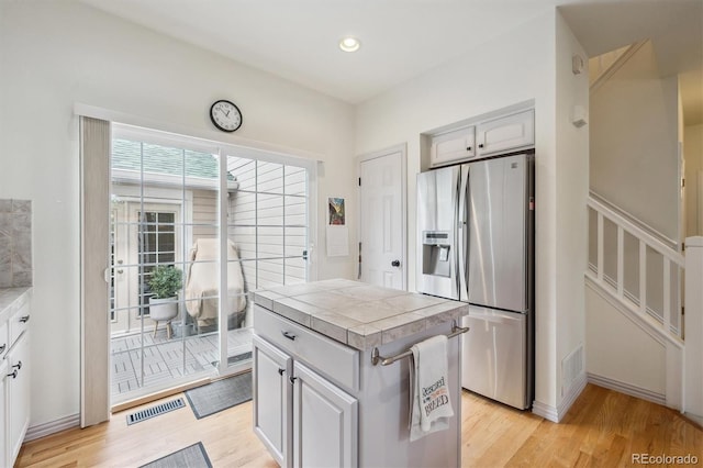 kitchen featuring visible vents, stainless steel fridge, tile counters, recessed lighting, and light wood finished floors