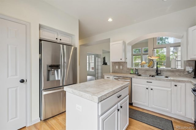 kitchen featuring decorative backsplash, arched walkways, a sink, stainless steel appliances, and white cabinetry