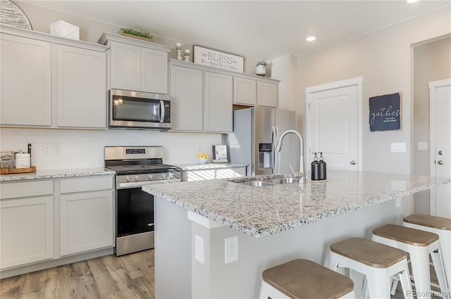 kitchen featuring a breakfast bar area, a sink, stainless steel appliances, light wood-style floors, and backsplash