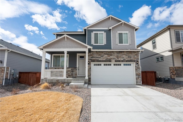 craftsman-style home with covered porch, concrete driveway, an attached garage, fence, and stone siding