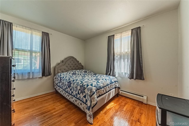 bedroom featuring a baseboard radiator, light wood-type flooring, and multiple windows