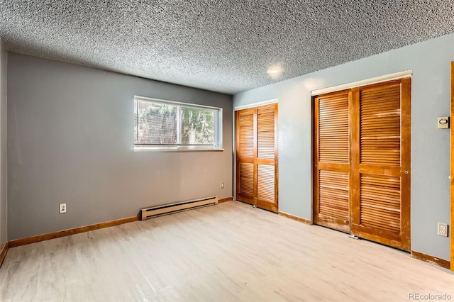 unfurnished bedroom featuring a baseboard heating unit, two closets, wood finished floors, a textured ceiling, and baseboards