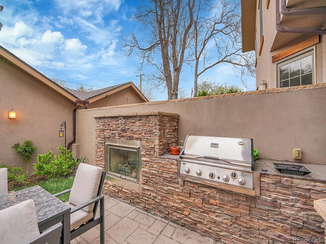 view of patio / terrace featuring an outdoor stone fireplace, exterior kitchen, and grilling area