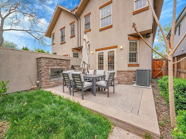 back of property featuring central air condition unit, an outdoor stone fireplace, french doors, and a patio