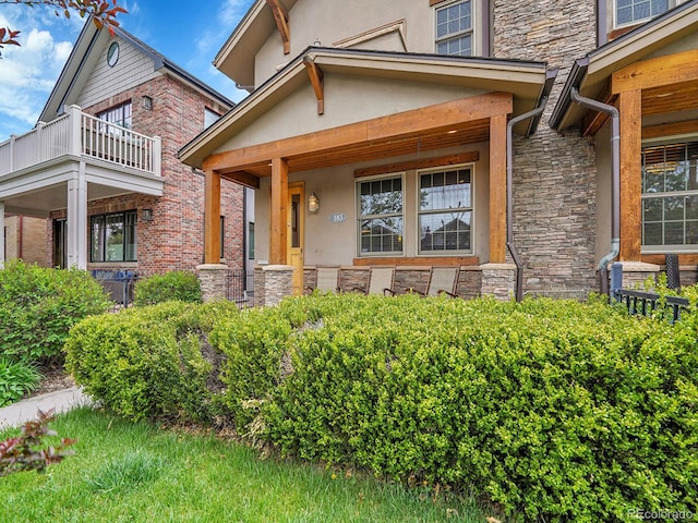 view of exterior entry featuring a porch, stucco siding, a balcony, and stone siding