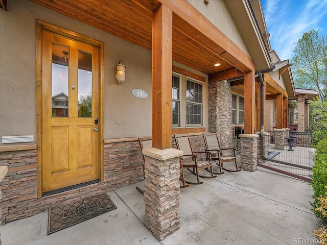 doorway to property with covered porch, stone siding, and stucco siding