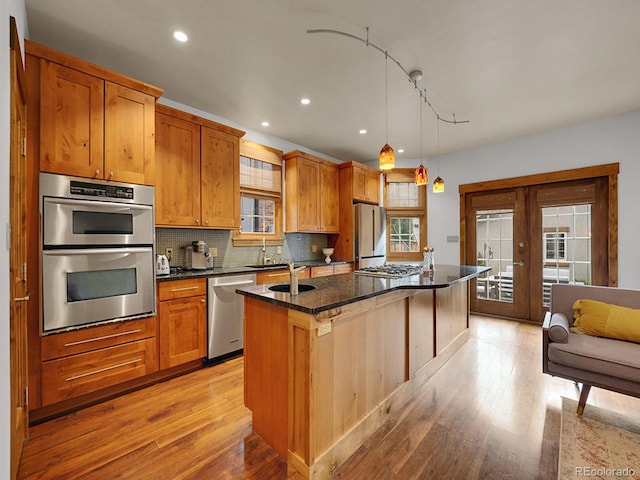 kitchen with a healthy amount of sunlight, a center island with sink, stainless steel appliances, and light wood finished floors