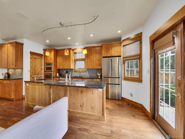 kitchen featuring appliances with stainless steel finishes, baseboards, decorative backsplash, wood finished floors, and a center island with sink