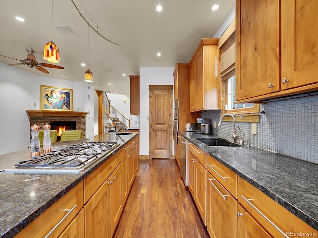 kitchen with brown cabinets, appliances with stainless steel finishes, a sink, dark wood finished floors, and a lit fireplace
