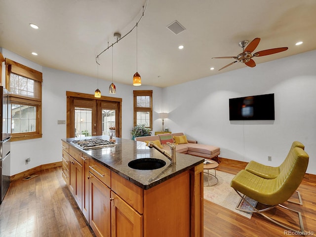 kitchen with a sink, stainless steel gas cooktop, wood-type flooring, baseboards, and visible vents