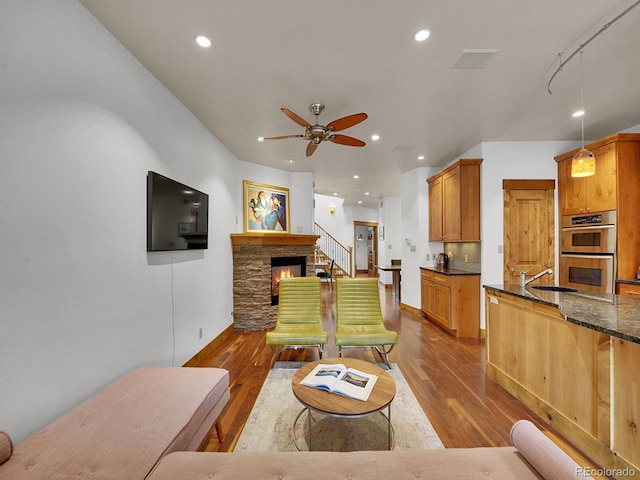 living room featuring dark wood-style flooring, a ceiling fan, recessed lighting, and a stone fireplace